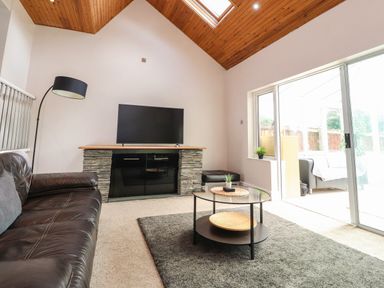 A living room with a leather sofa a TV on a stand a round glass coffee table and large sliding glass doors at Palm Court in Burton-in-Kendal
