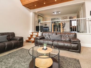 A living room with two brown leather sofas a glass coffee table stairs leading to a dining area with a wooden table and black chairs at Palm Court in Burton-in-Kendal