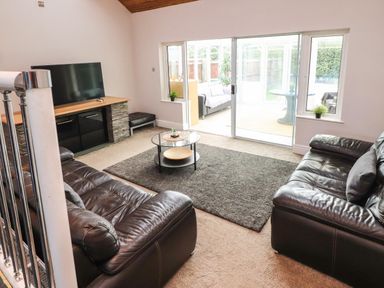 A living room with two leather sofas a glass coffee table a television and sliding glass doors at Palm Court in Burton-in-Kendal