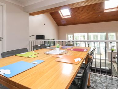 A dining table with colorful placemats and coasters in a room with a slanted wooden ceiling and skylights at Palm Court in Burton-in-Kendal