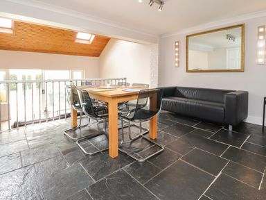 A dining area with a wooden table and black chairs next to a black leather sofa and a large mirror at Palm Court in Burton-in-Kendal