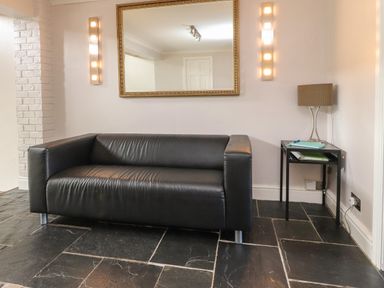 A black leather sofa with a side table holding a lamp and books under a wall mirror in a room at Palm Court in Burton-in-Kendal
