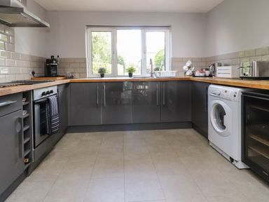 A kitchen with gray cabinets and wooden countertops a washing machine and oven under the counter at Palm Court in Burton-in-Kendal