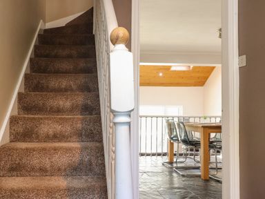 A carpeted staircase beside a dining area with a wooden table and clear chairs at Palm Court Burton-in-Kendal
