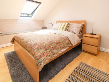 A bedroom with a wooden bed frame and colorful blanket under a skylight at Palm Court in Burton-in-Kendal