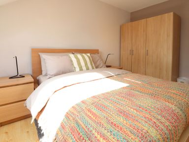 A bedroom with a bed with a colorful blanket and striped pillow beside wooden nightstands and a wardrobe at Palm Court in Burton-in-Kendal