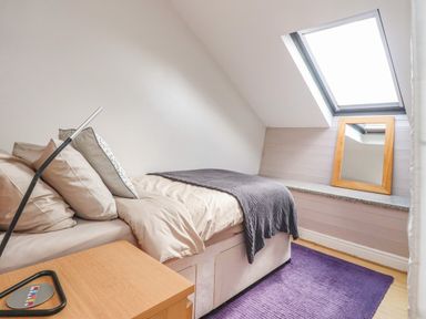 A bedroom with a single bed next to a window and a mirror on a ledge at Palm Court Burton-in-Kendal
