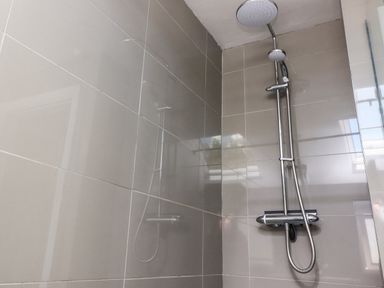 A shower area with a dual shower head and chrome fixtures on tiled walls at Palm Court in Burton-in-Kendal