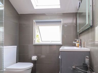A bathroom with a toilet a sink a mirror and an open window at Palm Court Burton-in-Kendal