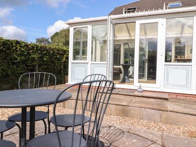 An outdoor patio area with a metal table and four chairs in front of a white conservatory at Palm Court in Burton-in-Kendal