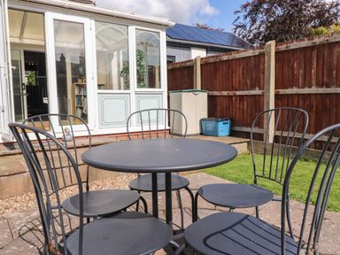 A black metal outdoor table with six chairs on a patio next to a conservatory and a wooden fence at Palm Court in Burton-in-Kendal