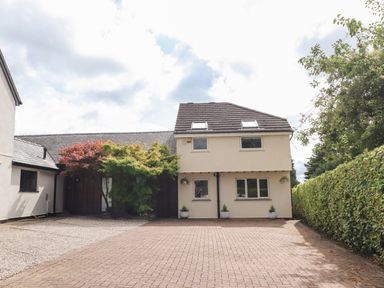 A detached house with a paved driveway and trees in front at Palm Court in Burton-in-Kendal