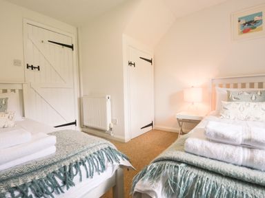A bedroom with two single beds with folded towels and blankets bedside table with lamp two white doors and a radiator at Lily Cottage in Looe