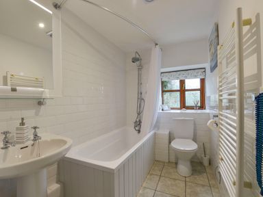 A bathroom with a bathtub shower combination sink toilet heated towel rack and a window at Lily Cottage in Looe