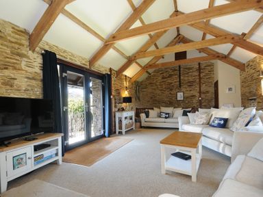 A living room with exposed wooden beams stone walls two sofas a coffee table a television and glass doors at Lily Cottage in Looe
