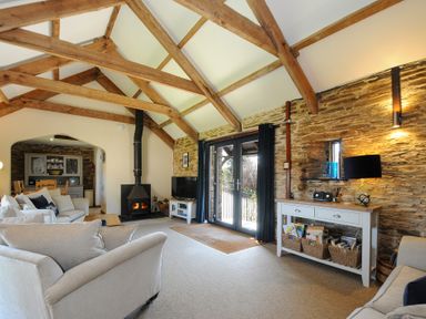 A living room with exposed wooden beams a wood burning stove sofas a wooden cabinet with baskets and a lamp at Lily Cottage in Looe