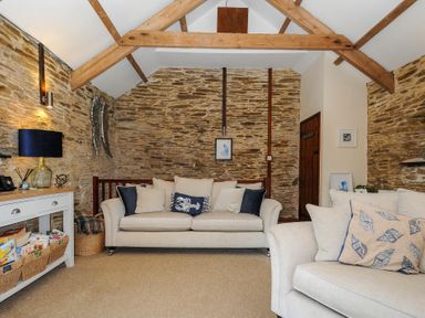 A living room with stone walls two beige sofas and wooden ceiling beams at Lily Cottage in Looe