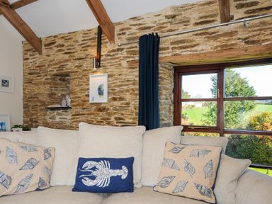 A living room with beige couch and decorative cushions by a window with stone wall at Lily Cottage in Looe