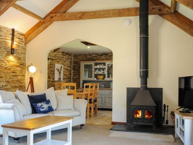 A living room with a sofa cushions coffee table wood stove and dining area with wooden chairs at Lily Cottage in Looe
