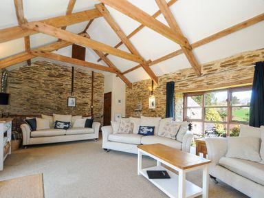 A living room with beige sofas wooden beams and a large window at Lily Cottage in Looe