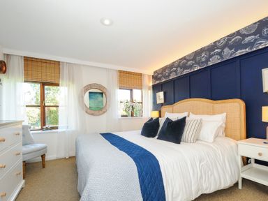 A bedroom with a double bed blue and white bedding wicker headboard and two windows with wooden blinds at Lily Cottage in Looe