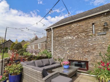 An outdoor seating area with a couch and flower pots at Lily Cottage in Looe