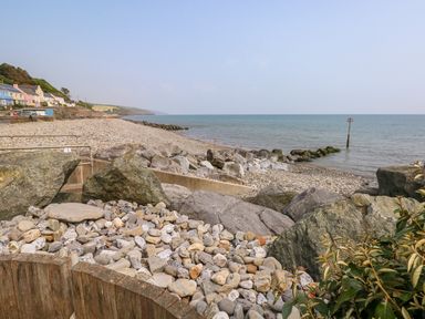 A pebble beach with large rocks and houses along the shore at Swn y mor in Amroth