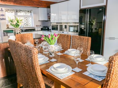 A kitchen with a wooden dining table set for six with woven chairs and a vase of tulips at Swn y mor in Amroth