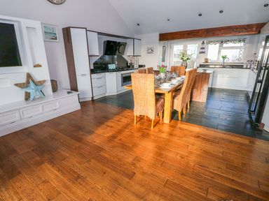 A kitchen and dining area with a wooden table set with dishes and chairs at Swn y mor in Amroth