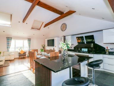 A kitchen and dining area with a black countertop island and dining table set near windows with curtains at Swn y mor in Amroth