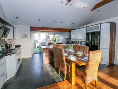 A kitchen with a dining table set with plates and glasses and woven chairs at Swn y mor in Amroth
