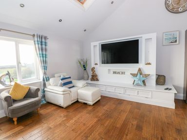 A living room with a gray armchair and a white leather chair next to a wall-mounted television and decorative items at Swn y mor in Amroth
