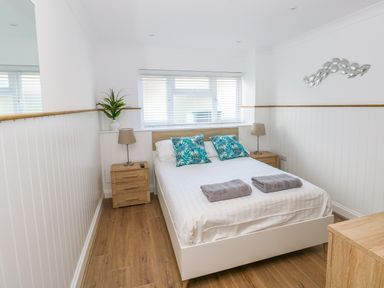 A bedroom with a double bed two bedside tables with lamps and a plant on one of them at Swn y mor in Amroth