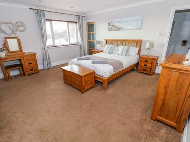 A bedroom with a wooden bed chest of drawers dressing table and bedside tables at Swn y mor in Amroth