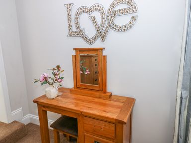 A wooden dressing table with a mirror and a vase with flowers underneath a wall decoration spelling love at Swn y mor in Amroth
