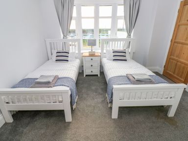 A bedroom with two single beds separated by a nightstand with a lamp and window at Swn y mor in Amroth