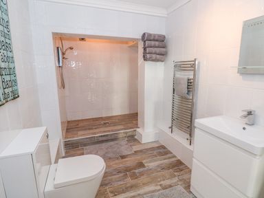 A bathroom with a toilet, sink, heated towel rack, folded towels, and a walk-in shower at Swn y mor in Amroth