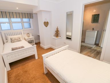 A bedroom with two single beds nightstand mirror and a bathroom visible through an open door at Swn y mor in Amroth