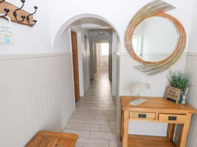 A hallway with a wooden table holding a fish sculpture and plant under a round mirror at Swn y mor in Amroth