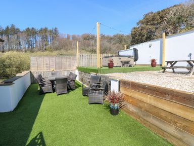 An outdoor patio area with wicker chairs a table a hot tub and wooden picnic table at Swn y mor in Amroth