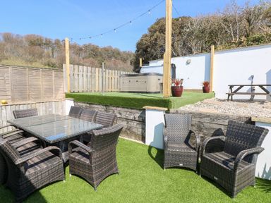 An outdoor seating area with wicker chairs and glass table on artificial grass with a hot tub and picnic table in the background at Swn y mor in Amroth