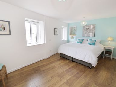 A bedroom with a double bed with turquoise pillows and white bedding two bedside tables with lamps and wooden flooring at Waverley House in Beaumaris
