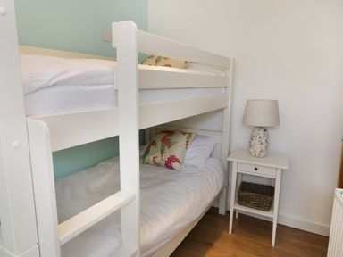 A bedroom with white bunk beds pillows a small table with a lamp and a basket on a wooden floor at Waverley House in Beaumaris