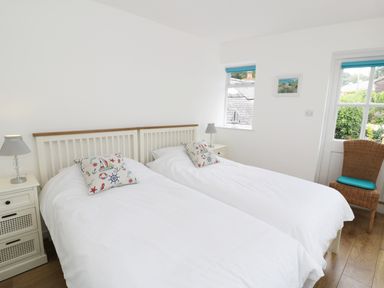 A bedroom with two single beds with white bedding two bedside tables with lamps a wicker chair by a window at Waverley House in Beaumaris