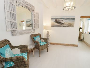 A room with two wicker chairs with blue cushions a small round table a large wall mirror and a painting of a boat at Waverley House in Beaumaris