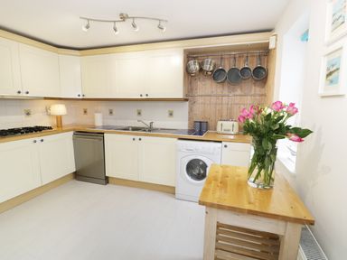 A kitchen with white cabinets a wooden countertop pots and pans hanging and flowers on a wooden table at Waverley House in Beaumaris