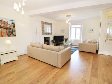 A living room with two beige sofas a glass coffee table flowers on the table wooden flooring a fireplace and a TV at Waverley House in Beaumaris