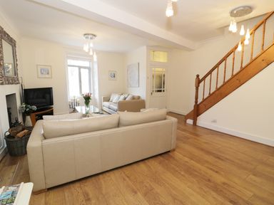 A living room with two beige sofas a television on a stand a glass coffee table and a wooden staircase at Waverley House in Beaumaris