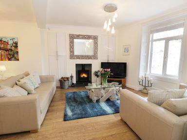 A living room with beige sofas a glass coffee table a blue rug a fireplace and a large window at Waverley House in Beaumaris