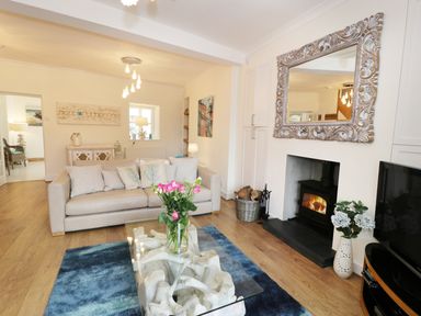 A living room with a beige sofa cushions a glass coffee table with flowers a fireplace and a large mirror at Waverley House in Beaumaris